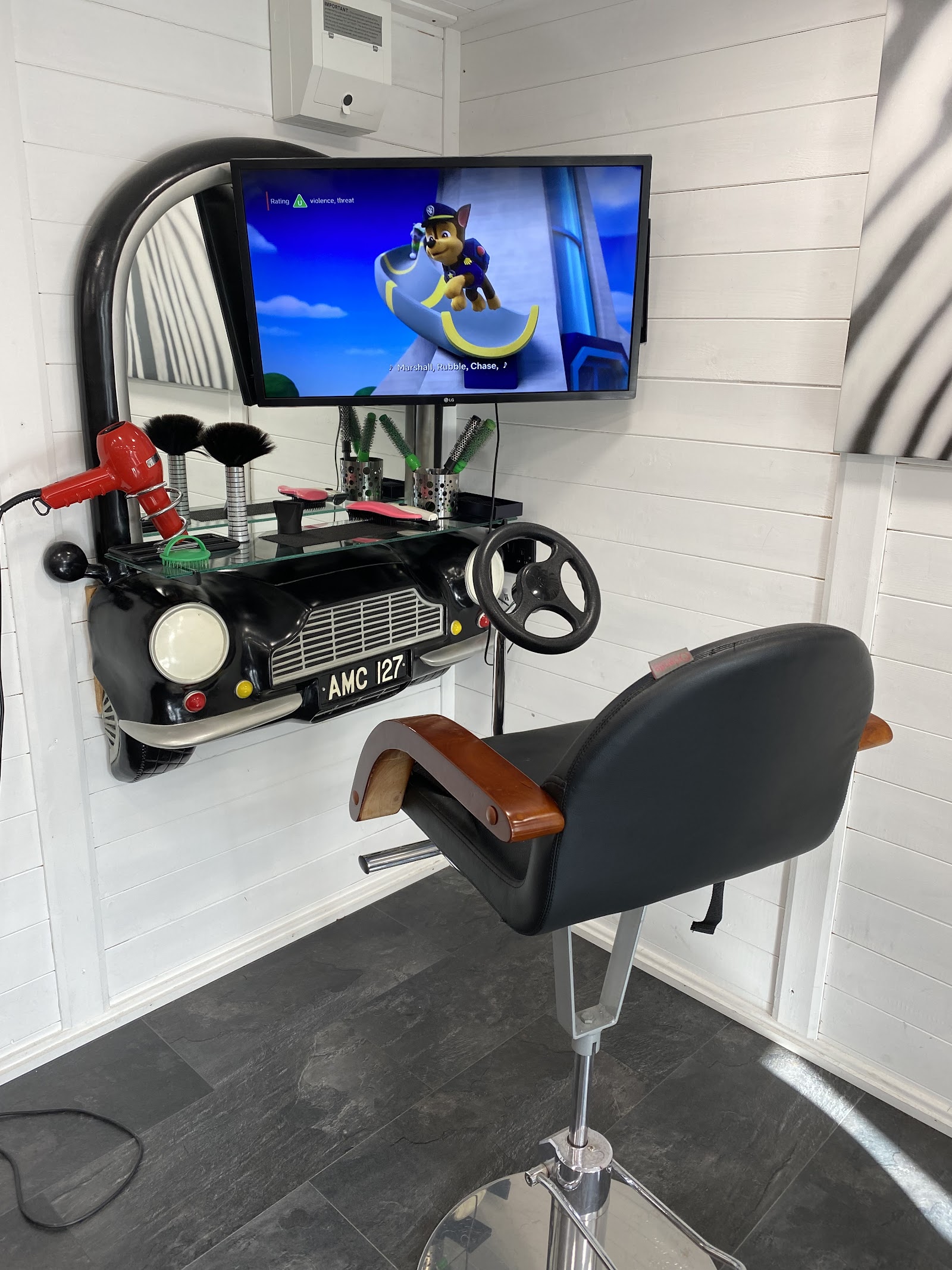 The children's station, a barber chair beside a classic-car mirror unit with a TV playing cartoons
