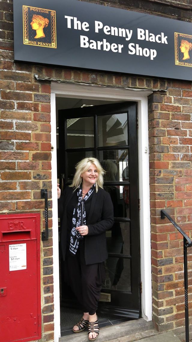 Owner Penny in the doorway beneath the Penny Black shop sign, beside the village postbox