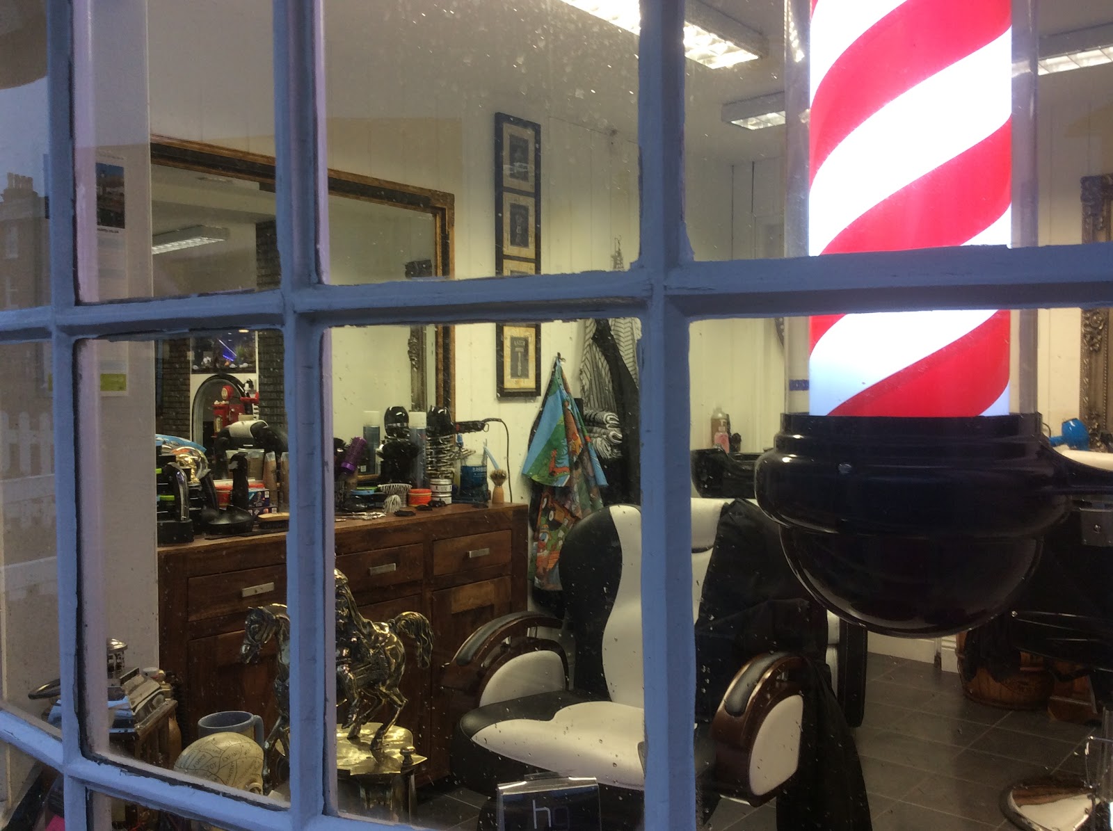 The view into the shop through a window, with vintage barber pole and traditional chairs